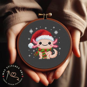 Könnte beinhalten: Ein Kreuzstichmuster mit einem niedlichen Axolotl, das einen roten und weißen Weihnachtshut und einen grünen Schal trägt. Das Axolotl ist von Schneeflocken auf einem dunkelgrauen Hintergrund umgeben.