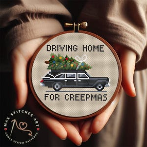 May include: Cross-stitch embroidery in a wooden hoop features a black hearse with a Christmas tree on top. The text reads "DRIVING HOME FOR CREEPMAS". The design is held in someone's hands.