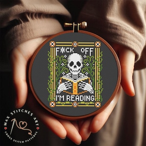 May include: A round embroidery hoop with a black background and a white skeleton holding a book. The text "F*CK OFF I'M READING" is written in a colorful font.