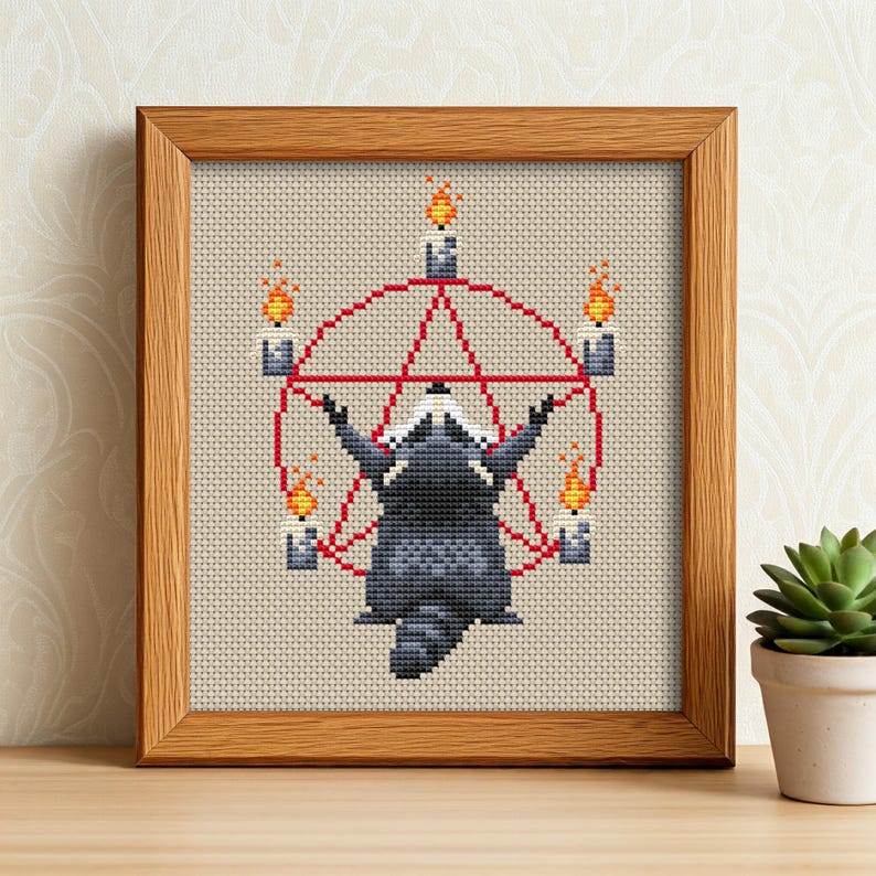 May include: Cross-stitch art of a raccoon with arms raised, centered within a red pentagram and circle, surrounded by lit candles. The artwork is framed in a wooden frame and set against a neutral background.