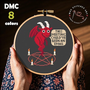 May include: Cross-stitch embroidery in a wooden hoop featuring a red devil with white horns and wings, standing on a pentagram. The text reads, "THIS MEETING COULD'VE BEEN AN EMAIL." The design uses 8 colors and is a Max Stitches Art cross-stitch pattern.