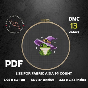May include: Cross-stitch pattern featuring a green frog wearing a purple witch hat with a gold buckle. The design is set in a wooden embroidery hoop. The text reads "DMC 13 colors" and "PDF". The pattern size is 3.14 x 2.64 inches.