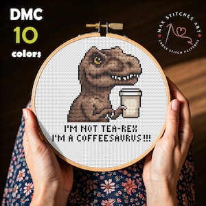 Może przedstawiać: Haft krzyżykowy w drewnianym tamborku, przedstawiający brązowego T-Rexa z filiżanką kawy. Tekst brzmi: "I'M NOT TEA-REX I'M A COFFEESAURUS!!!". Projekt wykorzystuje 10 kolorów.