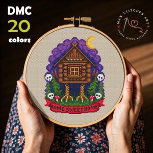 May include: Cross stitch pattern of a spooky house with legs, mushrooms, and skulls. The pattern is in a wooden embroidery hoop and says "Home Sweet Home".