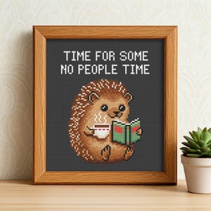 Könnte beinhalten: Ein gerahmtes Kreuzstich-Design mit einem Comic-Igel, der eine Tasse Kaffee und ein Buch hält. Der Text "Time for some no people time" befindet sich über dem Igel.