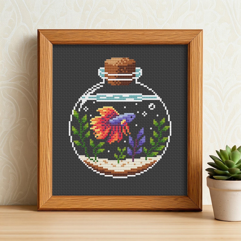 May include: A cross-stitch pattern of a glass bottle with a cork stopper, containing a colorful betta fish and green and purple plants. The bottle is on a dark gray background.