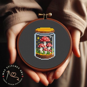 Puede incluir: Un patrón de punto de cruz de un frasco de vidrio con champiñones rojos y blancos en su interior. El frasco está sobre un fondo oscuro.