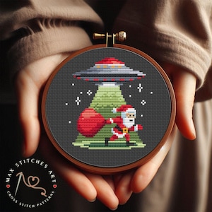 Puede incluir: Patrón de punto de cruz de Santa Claus sosteniendo una bolsa de regalos, volando en un OVNI. El OVNI es verde y tiene una luz roja en la parte superior. El fondo es azul oscuro con copos de nieve blancos.