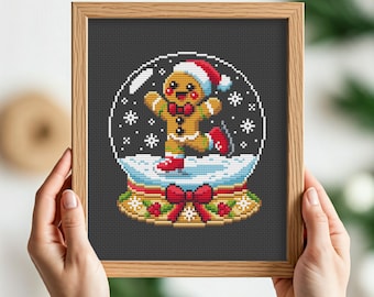 May include: A framed cross-stitch artwork featuring a gingerbread man in a snow globe. The gingerbread man wears a Santa hat and skates on ice. The snow globe sits atop a decorative base with a red bow. The background is dark gray.