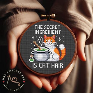 Könnte beinhalten: Ein schwarzes und weißes Kreuzstichmuster mit einer Katze, die einen Kessel umrührt, mit dem Text "Die geheime Zutat ist Katzenhaar".