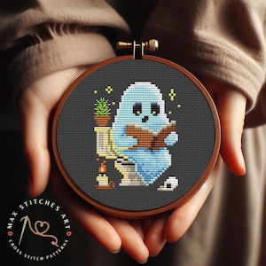 Op de afbeelding: Een kruissteekpatroon met een geest die op een toilet zit en een boek leest. De geest is blauw en wit, en het toilet is wit. Er staat een kleine plant in een pot naast het toilet.