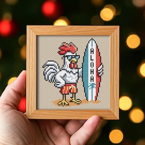 Puede incluir: Obra de arte de punto de cruz en un marco de madera. La imagen presenta un gallo pixelado con gafas de sol y pantalones cortos de baño, sosteniendo una tabla de surf con la palabra "ALOHA". El fondo es beige neutro.