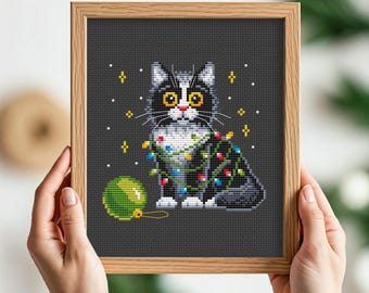 May include: Cross-stitch pattern of a black and white cat wearing Christmas lights and holding a green ornament.