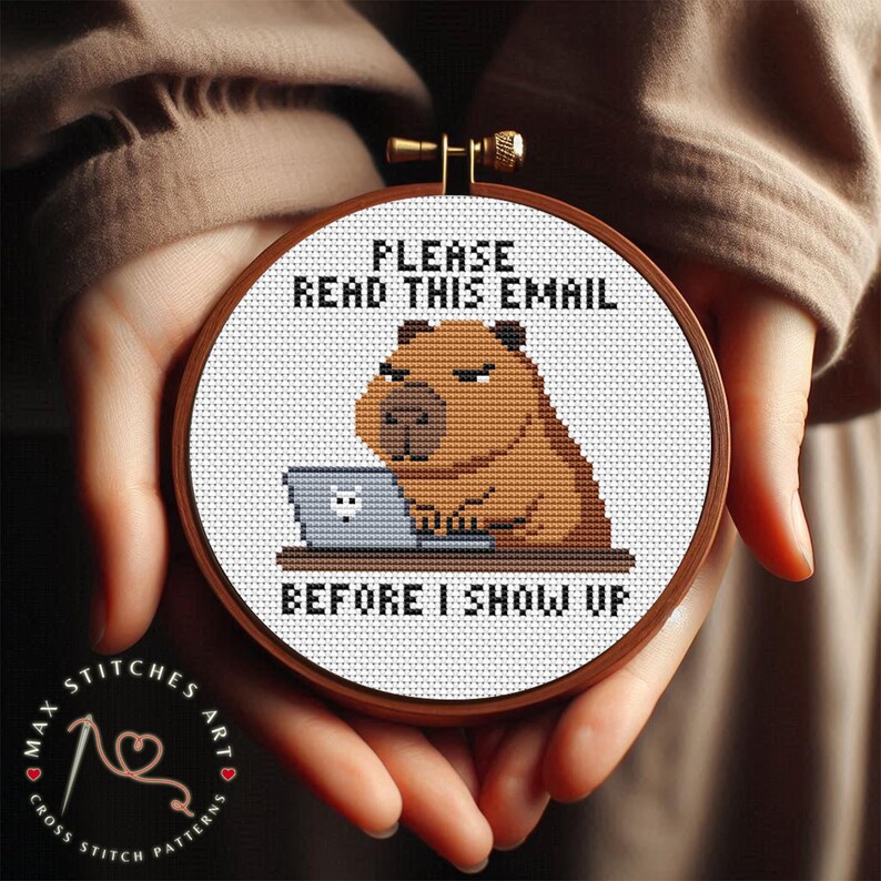 May include: A cross-stitch embroidery hoop featuring a brown capybara working on a laptop. The text reads "PLEASE READ THIS EMAIL BEFORE I SHOW UP." The hoop is held in hands, with the Max Stitches Art logo visible.