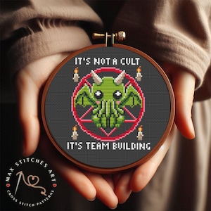 Könnte beinhalten: Ein runder Stickrahmen mit schwarzem Hintergrund und einem grünen Cartoon-Monster mit Tentakeln in einem roten Pentagramm. Der Text "IT'S NOT A CULT" befindet sich über dem Monster und "IT'S TEAM BUILDING" unter dem Monster.