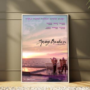 May include: A rectangular film poster for Spring Breakers showing a sunset over the sea, a white piano, and three figures in dark clothing. The title Spring Breakers is printed in black script, with names and review quotes in purple text.