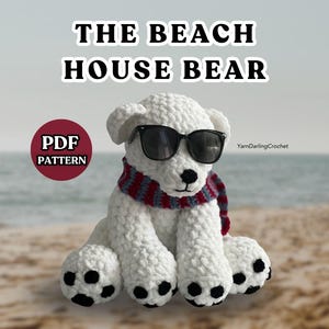 May include: A white crocheted bear plush toy wearing black sunglasses and a red and blue striped scarf. The bear has black paw pads and a black nose. Text reads THE BEACH HOUSE BEAR, PDF PATTERN, and YarnDarlingCrochet. The bear is sitting upright.