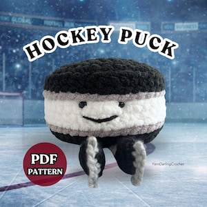 May include: A crocheted hockey puck plush toy with a black top and bottom, a white middle section, and thin grey stripes. It features a stitched black smile and two small black eyes. The text HOCKEY PUCK and PDF PATTERN are visible.