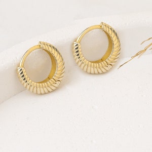 May include: A pair of gold hoop earrings with a textured, ribbed design. The earrings are on a white surface.