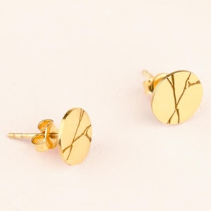 Może przedstawiać: Para złotych kolczyków z okrągłym wzorem o spękanej lub fakturowanej powierzchni.