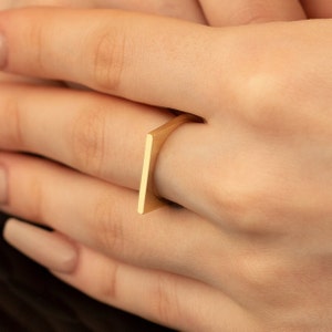 May include: A gold square ring with a unique design. The ring is open on one side and sits on the finger.