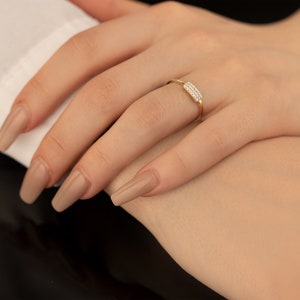 Könnte beinhalten: Ein goldener Ring mit einem rechteckigen Band aus kleinen, klaren Steinen.