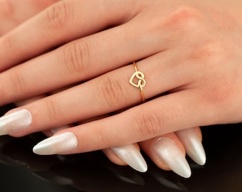 Può includere: Un anello d'oro con un design a forma di cuore infinito. L'anello è indossato su un dito con smalto bianco.