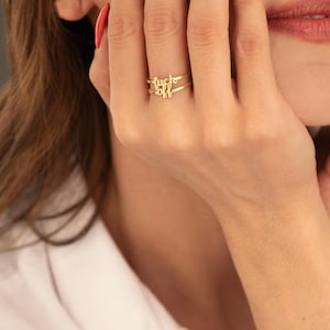 May include: A gold ring featuring the words "fuck off" in a cursive script. The ring is on a finger, with a close-up view. The jewelry is a fine, elegant piece.