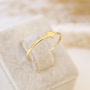 May include: A simple gold ring with a small star design. The ring is displayed on a white velvet box.