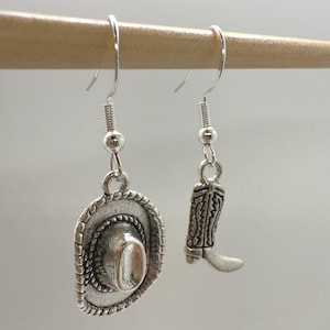 May include: Silver-toned cowboy hat and boot dangle earrings. The hat has a detailed brim and crown, while the boot features intricate embossed patterns. The earrings hang from silver-colored fish hook ear wires, perfect for a Western-themed look.