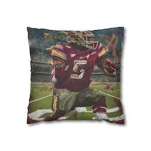 May include: A maroon and gold football player with the number 5 on their jersey runs on a green field with a blurred background. The player is wearing a helmet and has a determined expression on their face.