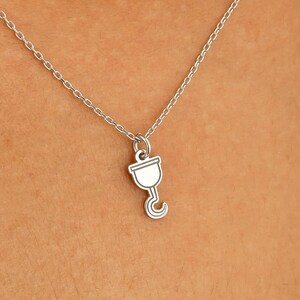 May include: Silver-toned necklace featuring a small pendant shaped like a menstrual cup. The pendant hangs from a delicate chain. The necklace is worn against a skin tone background.