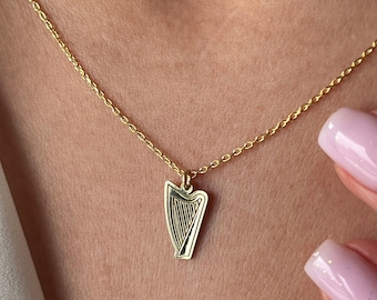 May include: A gold chain necklace with a small harp pendant. The harp is detailed with lines and is a traditional Irish symbol.