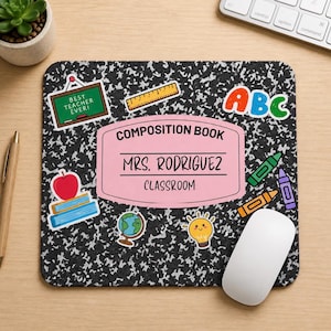 May include: A rectangular mousepad with a black and white speckled design, resembling a composition notebook. It features colorful stickers of school supplies and the text "COMPOSITION BOOK MRS. RODRIGUEZ CLASSROOM". A white computer mouse is on the right.