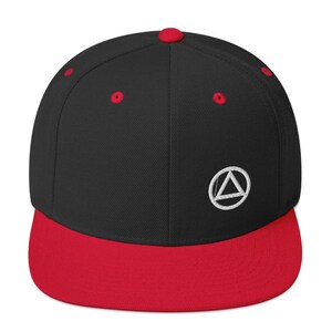 May include: A black baseball cap with a red brim and top button. The cap features a white embroidered symbol on the front. The hat is a flat-brim style, a popular streetwear accessory.