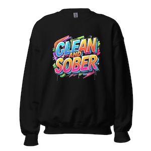 May include: Black sweatshirt with the words "CLEAN AND SOBER" in a colorful graffiti-style design. The text is in blue, orange, pink, and yellow, with green and purple accents. The sweatshirt has a crew neck and long sleeves.