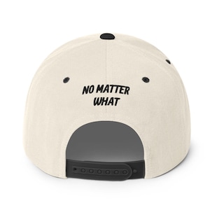 May include: A beige and black baseball cap with the text "NO MATTER WHAT" embroidered on the back.