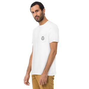 May include: White t-shirt with a pocket featuring a black circle with a triangle inside.