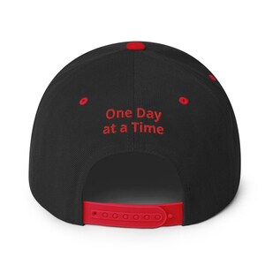 May include: Black and red baseball cap with the text "One Day at a Time" embroidered in red on the back.