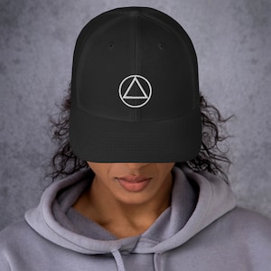 May include: A black mesh baseball cap with a white embroidered circle containing a triangle. The triangle has a circle inside of it.