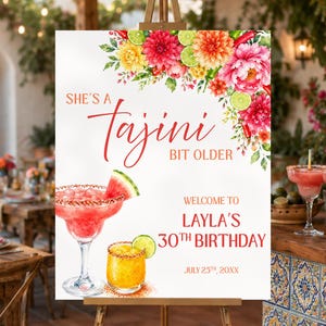 May include: A rectangular birthday welcome sign on a wooden easel featuring watercolor illustrations of flowers, limes, and chili peppers. The text reads: She's a Tajini bit older, Welcome to Layla's 30th Birthday, July 25th, 20XX, with cocktail graphics.