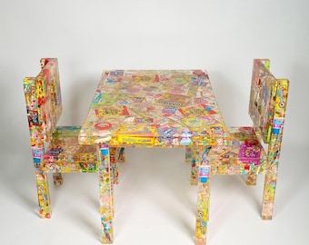 May include: A colorful table and two chairs made of clear resin with embedded candy wrappers. The table and chairs feature a variety of candy wrappers, including Skittles, Starburst, and Nerds.