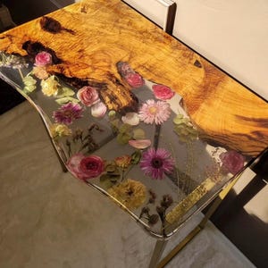 May include: A side table featuring a live edge wooden top and a clear resin section with embedded flowers. The table has a gold-coloured metal frame, creating a modern look. The wood grain is visible. The table's dimensions are in centimetres.