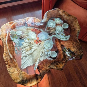 Könnte beinhalten: Einzigartiger Couchtisch mit natürlicher Kante und natürlicher Holzmaserung. Die Tischoberfläche ist mit Trockenblumen, weißen Rosen und kleinen weißen Tassen eingelegt. Ein warmes, einladendes Möbelstück.