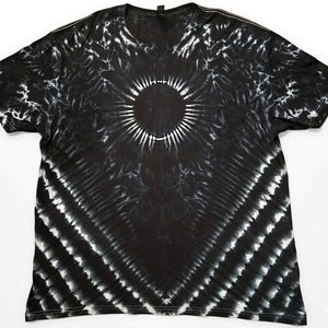 Könnte beinhalten: Schwarz-weißes T-Shirt mit Batikmuster und einem kreisförmigen Design in der Mitte. Das Shirt hat einen Rundhalsausschnitt und kurze Ärmel. Das Batikmuster weist strahlenförmige Linien und einen Sonnenstrahleffekt auf.
