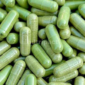 May include: A close-up of many green capsules, possibly supplements or medication. The capsules are cylindrical with rounded ends, filled with a green powder. The lighting highlights the texture and colour variations of the capsules.