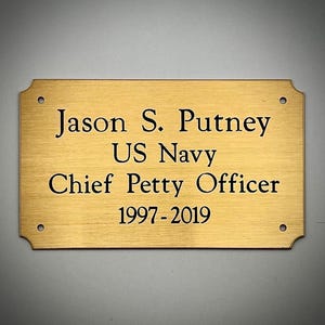 May include: A rectangular brass plaque with rounded corners and four screw holes. The plaque features the engraved text "Jason S. Putney, US Navy, Chief Petty Officer, 1997-2019" in black font.