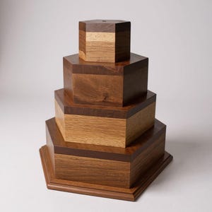Puede incluir: Una pila de cuatro cajas hexagonales de madera de diferentes tamaños. Las cajas están hechas de diferentes tipos de madera, con una mezcla de tonos marrones claros y oscuros. Las cajas están dispuestas en una formación escalonada, con la caja más pequeña en la parte superior.