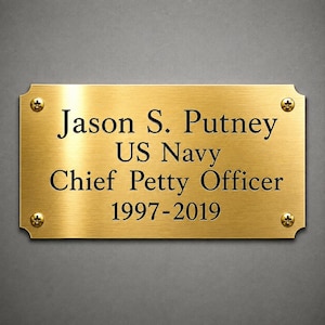 May include: A rectangular gold-toned metal plaque with rounded corners and four mounting screws. The engraved black text reads: Jason S. Putney, US Navy, Chief Petty Officer, 1997-2019. The surface has a brushed metallic finish.