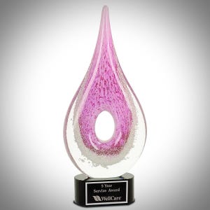 Op de afbeelding: Een roze glazen award in de vorm van een traan met een gat in het midden. De award staat op een zwarte basis met een plaquette waarop staat "5 Year Service Award WellCare".
